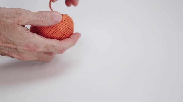 Hands unrolling a ball of orange string in close-up on a blank white surface
