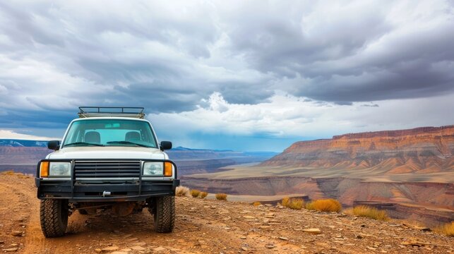 A sturdy white off road SUV sits at the edge of a remote rocky canyon overlook  The scene is set against a backdrop of dramatic stormy clouds and expansive arid landscape