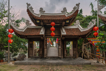 Obraz premium Traditional wooden entrance gate of Thuy Trung Tien Temple decorated with red lanterns and a stone bridge leading to the pagoda in Hanoi, Vietnam