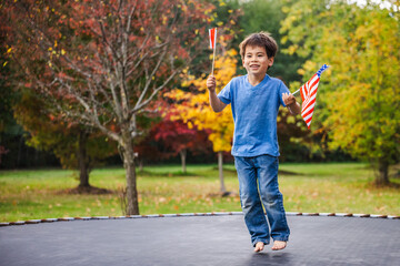 Fototapeta premium Smiling Boy Jumping Barefoot With American and Red-and-White Flags