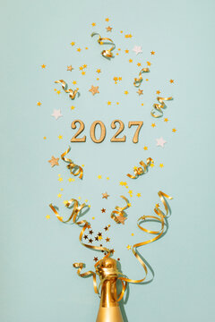 2027 splash or fireworks from glittering numbers, serpentine streamers and glittering stars for New Year celebration with golden champagne bottle top view, vertical.