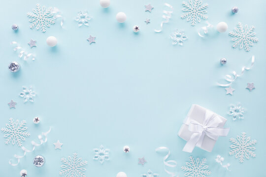Festive Christmas and New Year holiday snowy composition frame with white snowflakes, silver baubles, gift box and winter decoration tinsel top view.