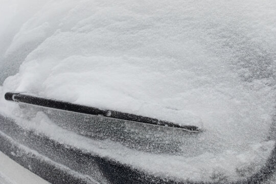 Car rear window with windscreen wipers are covered with snow after heavy winter snowfall. Natural disasters and climate change.