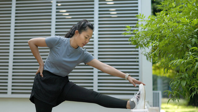 Asian Sportswoman Performing Standing Hamstring and Leg Stretch on Railing Outdoor Park Workout
