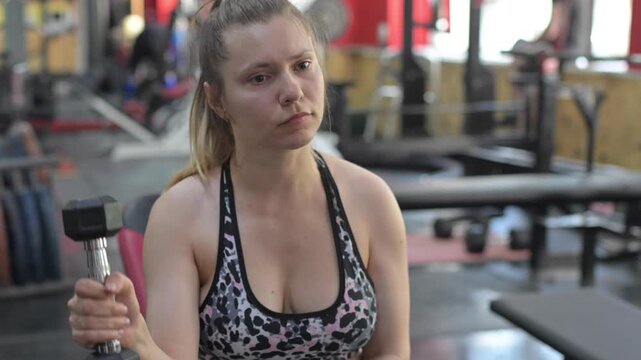 A Caucasian woman with cerebral palsy exercises with dumbbells in a gym.