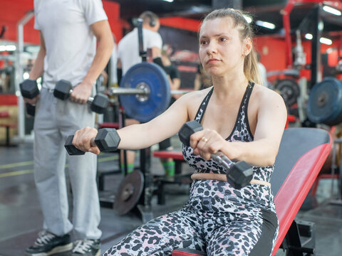 A Caucasian woman with cerebral palsy exercises with dumbbells in a gym.