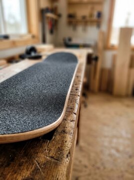 Handcrafted Skateboard Deck Resting on a Rustic Wooden Workbench in a Serene Artisan Workshop Setting Captured with Soft Natural Light and Depth of Field