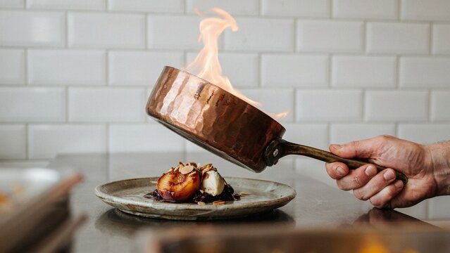Chef flambeing roasted plum dessert with ice cream in copper pan