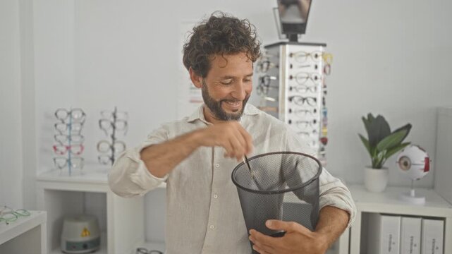 Man places eyeglass frames into a mesh paper bin while smiling and giving a thumbs up in an optician studio; satisfaction.