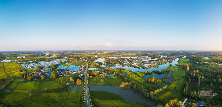 An aerial shot showcases a vast rural landscape with farmland, waterways, and scattered settlements under a clear blue sky.