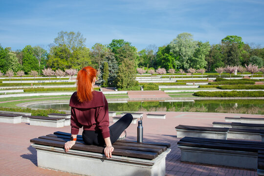 Sporty active ginger woman on the bench in public city park in the