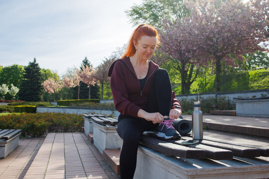 Middleaged ginger woman tying shoelaces before morning jogging in