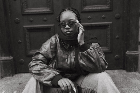 Stylish young Black woman in sunglasses sits on city steps