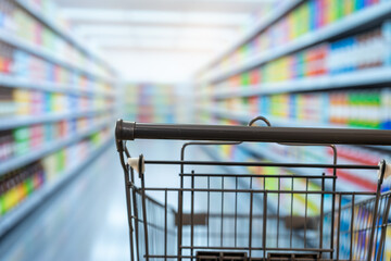 Empty shopping cart in a bright supermarket aisle with blurred shelves full of colorful grocery products, showing a retail shopping experience. © NanSan