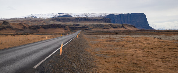 Empty Asphalt Road Leading Towards Snow-Capped Basalt Mountains in Iceland © Sonja