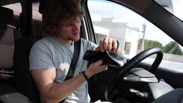 Car ownership drains the drivers budget as frequent maintenance repairs and running costs consume money leaving him frustrated while checking his empty wallet in the cars
