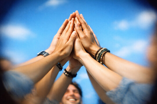Friendly group holding hands together, symbolizing unity and peace. Blurred natural backdrop emphasizes focus on hands.