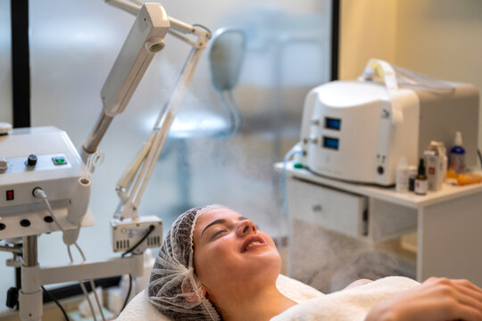 Young relaxed woman receiving warm steam facial treatment from professional steamer