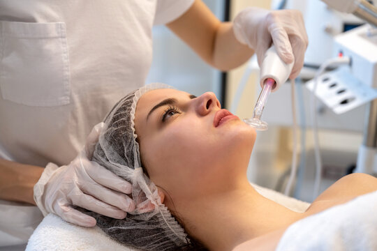 Close up portrait of female client receiving darsonvalization skin treatment on chin