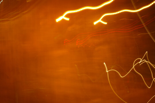 Abstract long exposure photograph showing bright yellow and red light trails glowing against a dark warm amber background with dynamic camera motion.