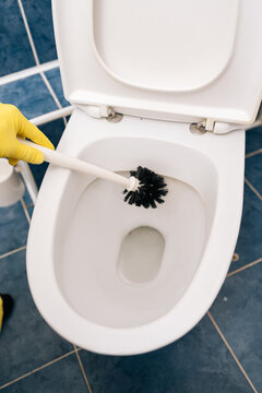 Top view of person hand in yellow protective glove cleaning ceramic toilet bowl with brush, maintaining cleanliness and hygiene standards in residential or commercial washroom environment.