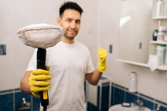 Selective focus of young man in yellow gloves holding active steam cleaner, cleaning surfaces in modern bathroom, focusing on eco-friendly sanitation and maintaining spotless home environment.