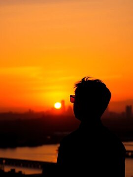 Silhouette of a figure gazing at an orange sunset sky with city skyline in the background, sunsets, misty