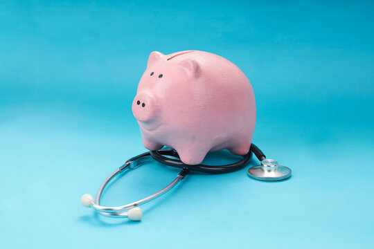 Healthcare Cost Concept with Pink Piggy Bank and Stethoscope Over Blue Background