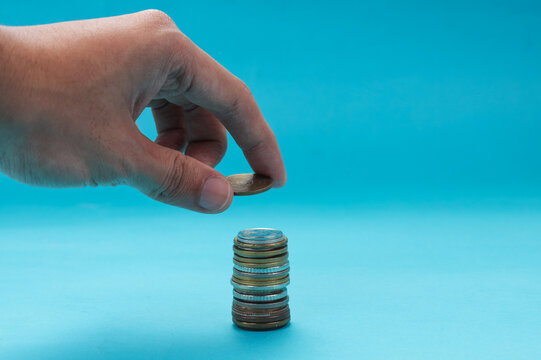 Hand Putting Coins Money Against Blue Background
