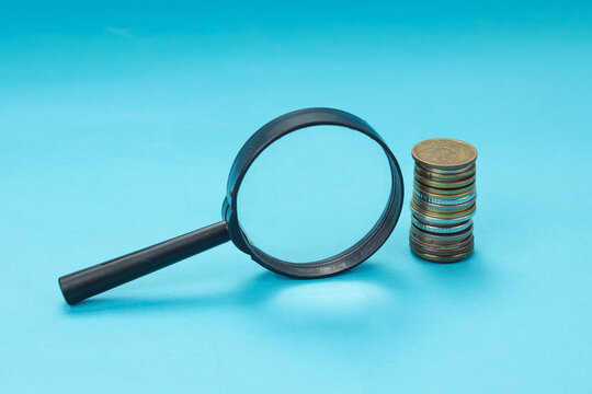 High Angle of Magnifying Glass Beside Stacked Coins on Blue Background