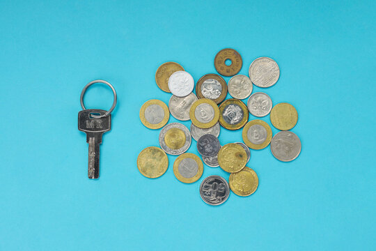 Top View of Metal Key Beside Scattered Coins Against Blue Background