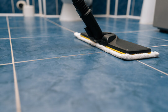 Steam cleaner sanitizing blue tiled bathroom floor, releasing steam for deep cleaning and hygiene, maintaining fresh and disinfected home environment. Concept of household chores and housework.