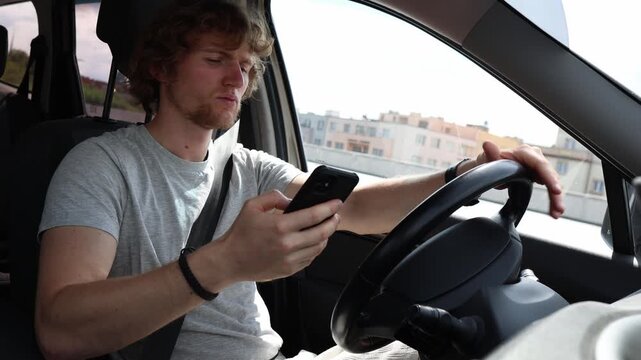 Young driver stares at his smartphone while driving through the city losing focus on the road as phone distraction creates dangerous behavior and high accident risks here