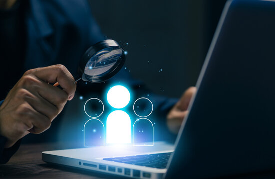 Business professional using magnifying glass with people icons on laptop, representing recruitment, talent search, candidate screening, human resources, and online workforce management.
