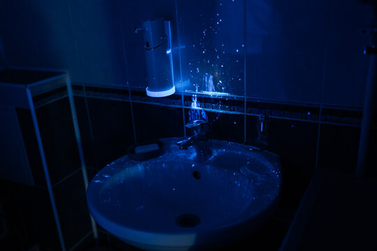 Analyzing bathroom hygiene with ultraviolet light revealing invisible traces of dirt, bacteria, germs, and contamination on surfaces like sink and soap dispenser during cleaning inspection.