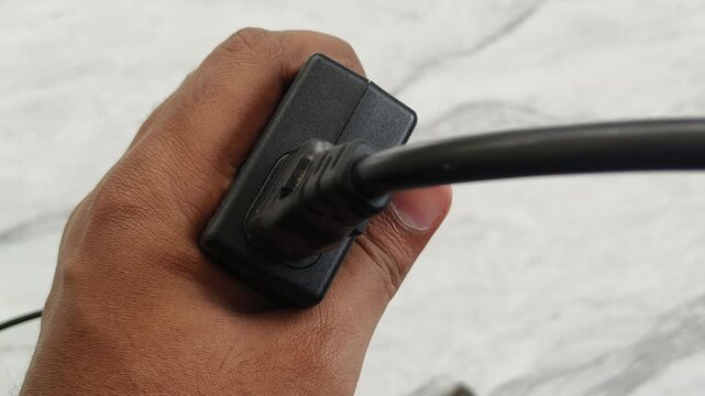 Hand plugging, connecting or input a black old traditional charging cable inside laptop computer charger adapter pin type port hole isolated on white background. Closeup top view.
