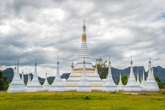 White pagodas of Toh Tae Ploe in Kayin State, Myanmar, set against lush green fields and scenic mountains under a cloudy blue sky with grazing cattle.