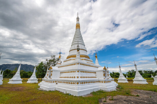 White pagodas of Toh Tae Ploe in Kayin State, Myanmar, set against lush green fields and scenic mountains under a cloudy blue sky with grazing cattle.