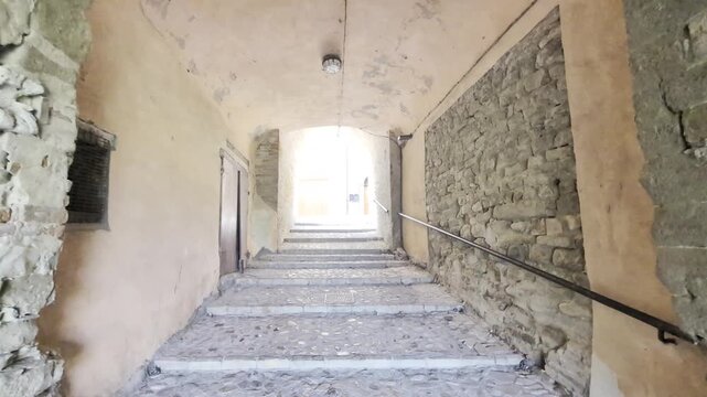 Una suggestiva scalinata in pietra attraversa un passaggio coperto ad arco, guidando lo sguardo verso la luce in un antico borgo italiano
