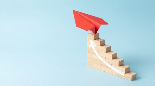 Red paper airplane taking off from a wooden staircase with an upward arrow on a blue background, symbolizing business growth and success.