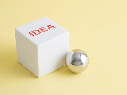 White cube labeled IDEA beside chrome sphere labeled REALITY ideal for business design symbolizing turning creative thought into tangible results