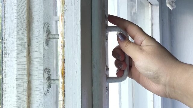 Woman checking for cold drafts coming through gaps in an old wooden window, air leaking through cracks, window sealing and home insulation in cold weather.