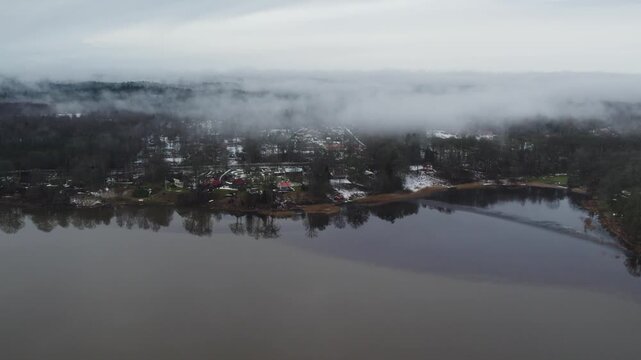 Grafsnas and Lake Anten across calm water with snowy wooded shoreline in Sweden, aerial dolly as low clouds hang over forest