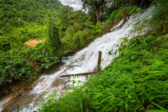 Scenic limestone cascading waterfall at Naw Ta or No Taw in Karen State, Myanmar, surrounded by lush green tropical forest, natural mountain cliff, and flowing stream in daylight.