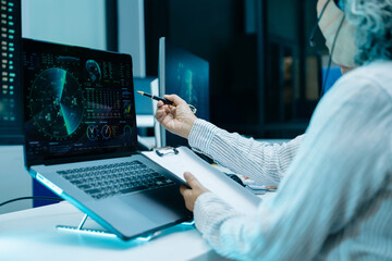 Asian engineer in headset analyzes radar screens and takes notes in a high tech control room