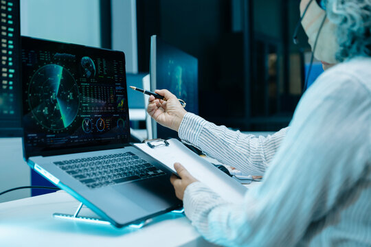 Asian engineer in headset analyzes radar screens and takes notes in a high tech control room