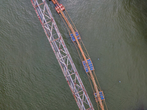 Aerial View of Water Pipeline Bridge Crossing a River Beside a Floating Bamboo Service Bridge Used by Workers in Indonesia, Captured from Above.