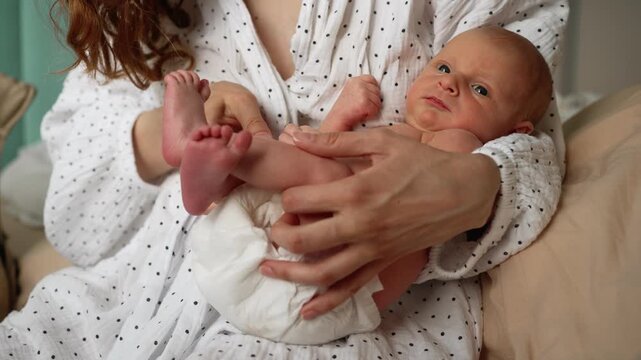 Young mother gently holding her newborn baby in her arms and doing therapeutic exercises by moving the infant's legs to help with colic, gas relief, and digestive health