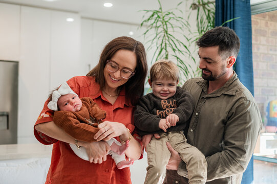 Happy parents holding their newborn baby and toddler son inside their home