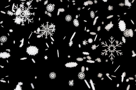 Snowflakes drift down against a black background in a three-dimensional representation. The scene shows various shapes and sizes of snowflakes creating a winter feel